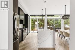 Kitchen featuring expansive windows, modern cabinets, gas range oven, stainless steel refrigerator with ice dispenser, and hanging light fixtures -