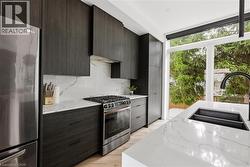 Kitchen featuring modern cabinets, appliances with stainless steel finishes, light stone counters, backsplash, and expansive windows -