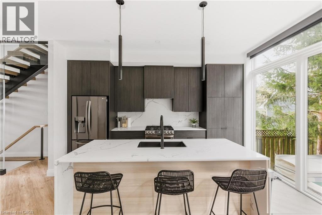 Kitchen featuring modern cabinets, light stone countertops, appliances with stainless steel finishes, a center island with sink, and expansive windows - 26 Huron Street, Grand Bend, ON - Indoor Photo Showing Kitchen With Stainless Steel Kitchen With Upgraded Kitchen