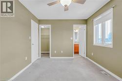 Unfurnished bedroom with light colored carpet, a walk in closet, a ceiling fan, and ensuite bathroom -