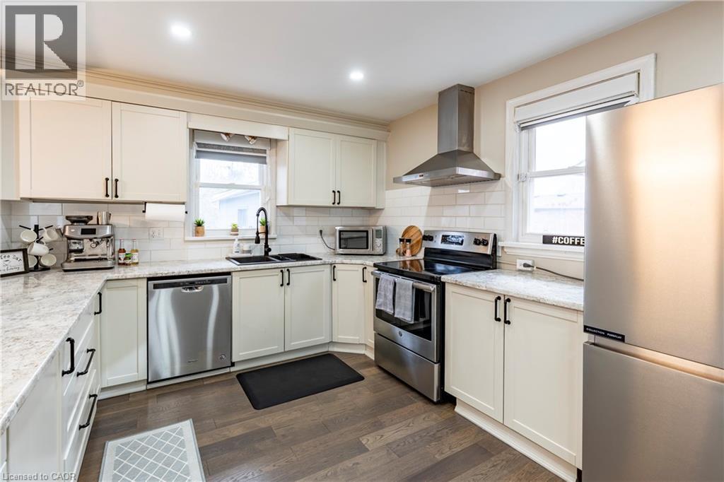 Kitchen featuring appliances with stainless steel finishes, wall chimney exhaust hood, dark wood-style floors, white cabinetry, and light stone countertops - 266 Melrose Avenue, Kitchener, ON - Indoor Photo Showing Kitchen With Double Sink With Upgraded Kitchen