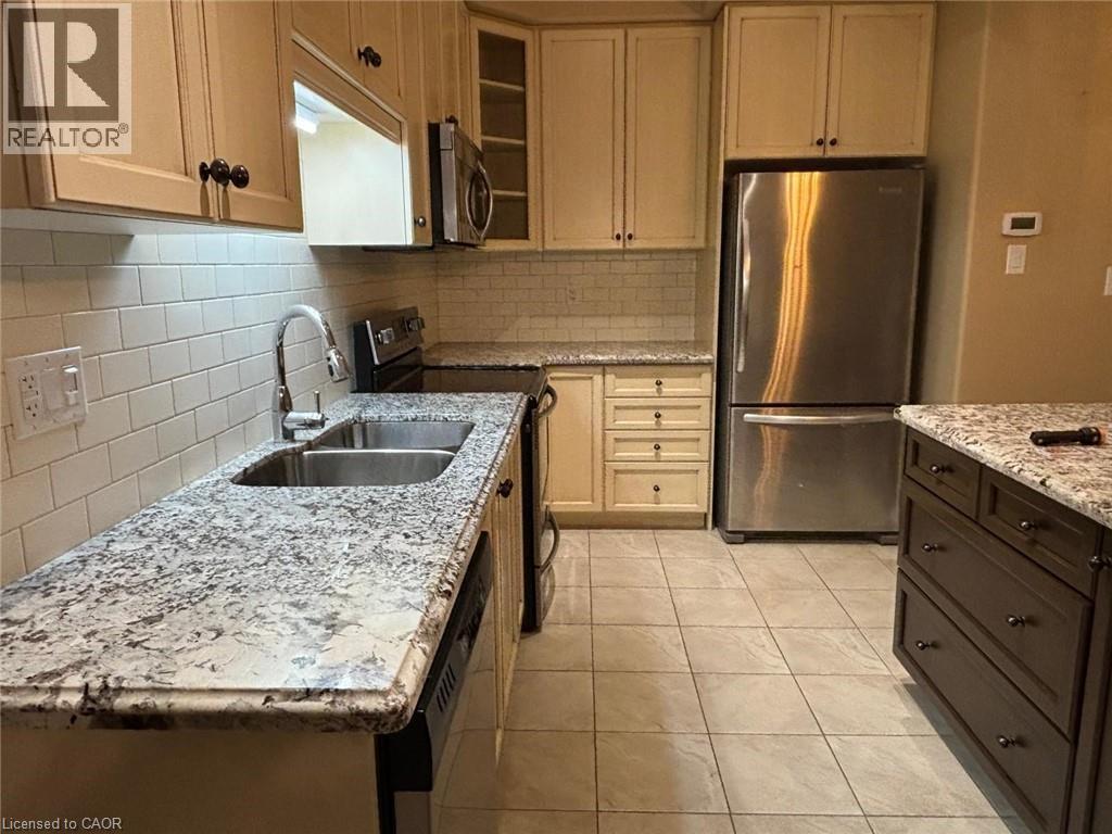 Kitchen featuring stainless steel appliances, glass insert cabinets, light stone counters, decorative backsplash, and light tile patterned floors - 6 Chestnut Drive Unit# 16, Grimsby, ON - Indoor Photo Showing Kitchen With Double Sink With Upgraded Kitchen