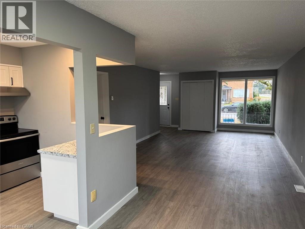Kitchen with stainless steel electric range, wood finished floors, under cabinet range hood, white cabinets, and a textured ceiling - 316 Dufferin Street, Stratford, ON - Indoor