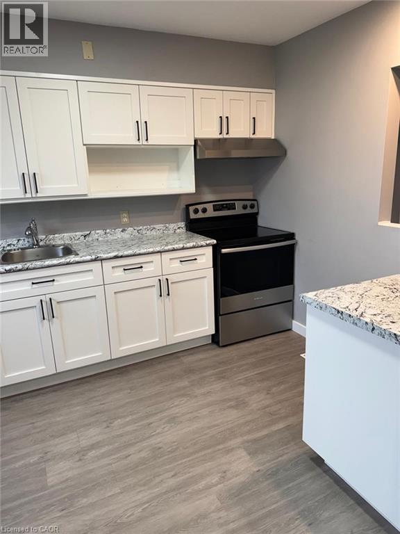 Kitchen featuring stainless steel range with electric stovetop, white cabinets, light stone counters, under cabinet range hood, and light wood-style floors - 316 Dufferin Street, Stratford, ON - Indoor Photo Showing Kitchen