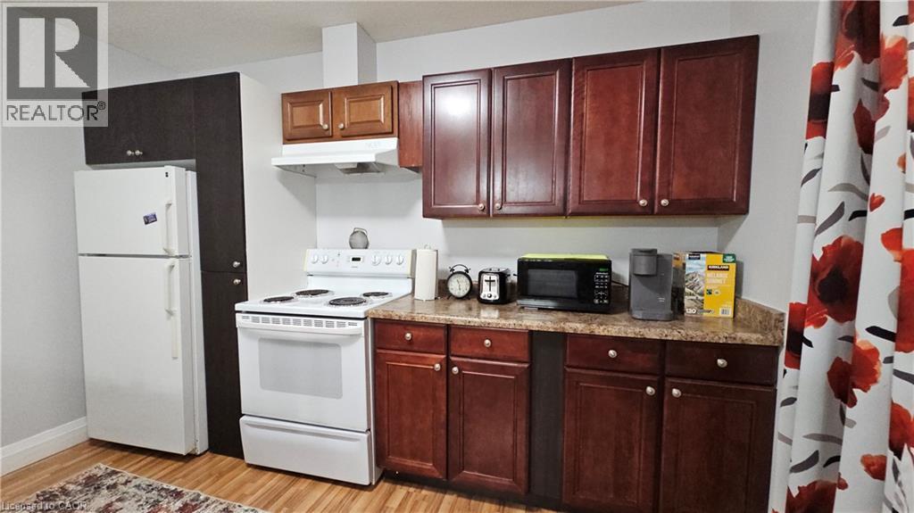 Kitchen with white appliances, under cabinet range hood, light wood-type flooring, light countertops, and dark brown cabinetry - 10 Doll Court, Kitchener, ON - Indoor Photo Showing Kitchen