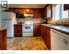 Kitchen with white appliances, light countertops, under cabinet range hood, and stone finish floors -