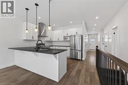 Kitchen with appliances with stainless steel finishes, wall chimney exhaust hood, dark wood-style floors, hanging light fixtures, and white cabinets -