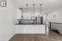 Kitchen with a peninsula, white cabinets, freestanding refrigerator, decorative light fixtures, and dark wood finished floors -