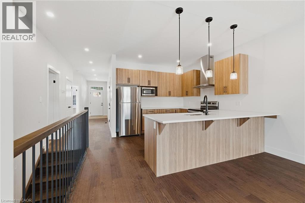Kitchen featuring a breakfast bar, stainless steel appliances, wall chimney range hood, a peninsula, and dark wood-type flooring - 4 Elgin Street W, Norwich, ON - Indoor Photo Showing Kitchen With Stainless Steel Kitchen With Upgraded Kitchen
