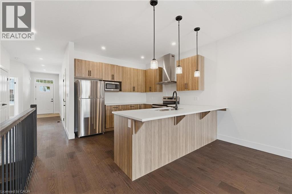 Kitchen with appliances with stainless steel finishes, a breakfast bar area, a peninsula, wall chimney range hood, and dark wood finished floors - 4 Elgin Street W, Norwich, ON - Indoor Photo Showing Kitchen With Stainless Steel Kitchen With Double Sink With Upgraded Kitchen