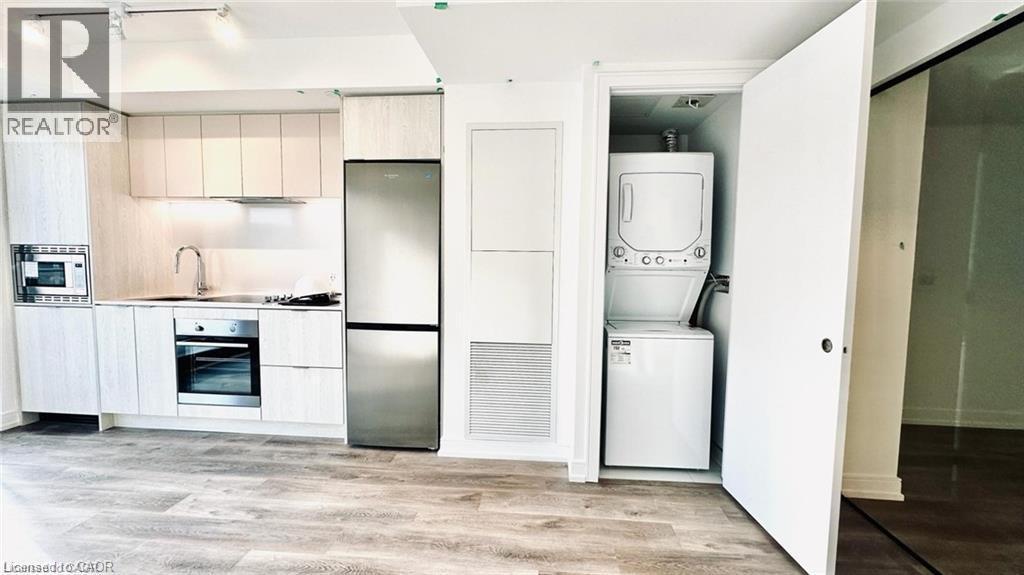 Kitchen featuring appliances with stainless steel finishes, light countertops, stacked washer and clothes dryer, light wood-style floors, and modern cabinets - 1 Jarvis Street Unit# 509, Hamilton, ON - Indoor Photo Showing Laundry Room
