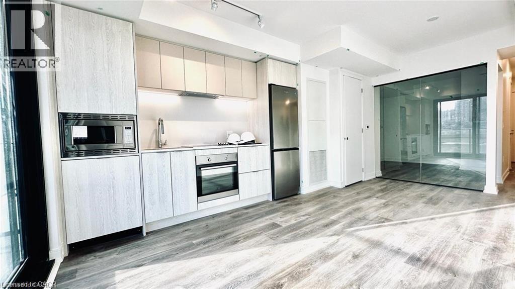 Kitchen featuring appliances with stainless steel finishes, light wood-style flooring, light countertops, cream cabinetry, and rail lighting - 1 Jarvis Street Unit# 509, Hamilton, ON - Indoor Photo Showing Kitchen