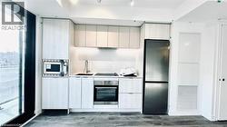 Kitchen featuring appliances with stainless steel finishes, dark wood-type flooring, light countertops, modern cabinets, and under cabinet range hood -