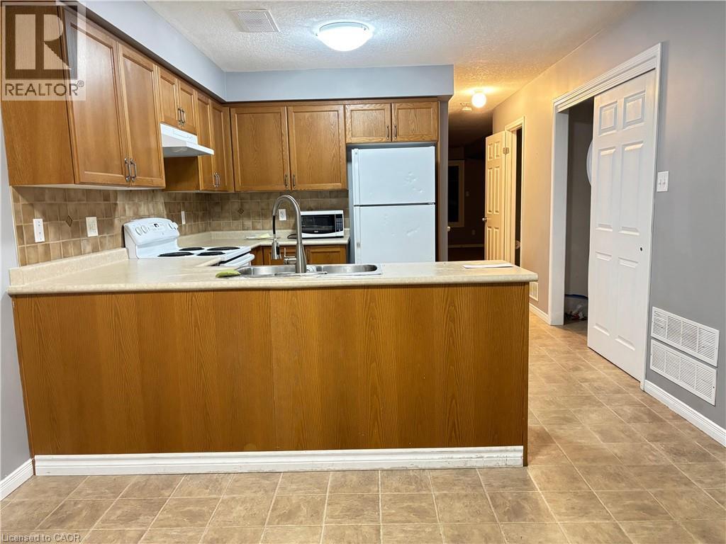 Kitchen with brown cabinetry, light countertops, white appliances, backsplash, and a peninsula - 50 Howe Drive Unit# 12A, Kitchener, ON - Indoor Photo Showing Kitchen