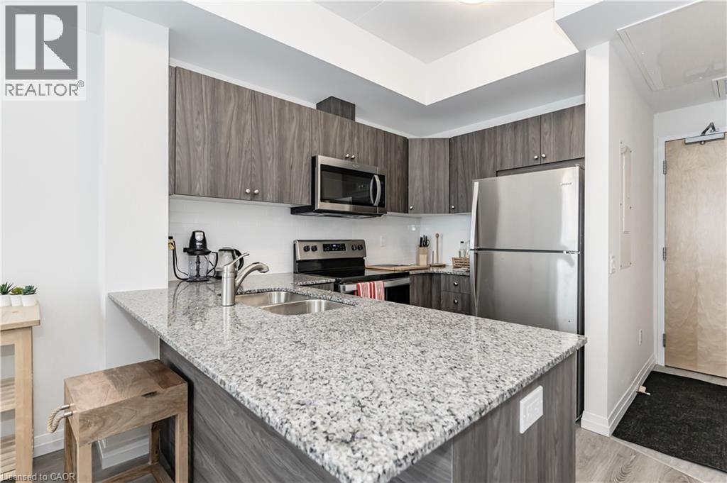Kitchen with light stone counters, appliances with stainless steel finishes, dark brown cabinetry, a peninsula, and modern cabinets - 60 Charles Street Unit# 2003, Kitchener, ON - Indoor Photo Showing Kitchen With Double Sink With Upgraded Kitchen