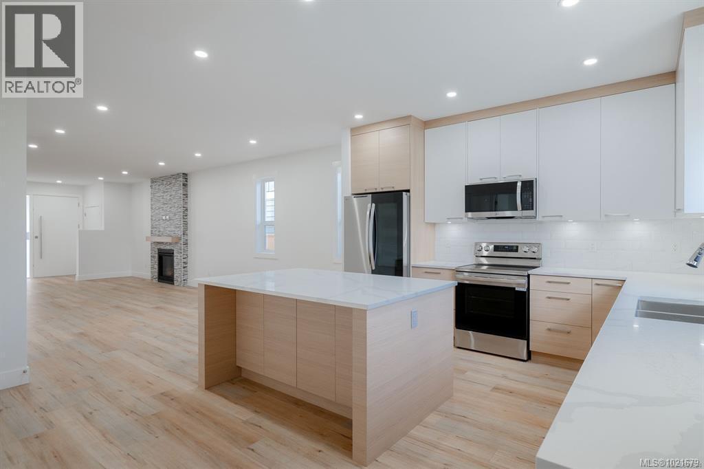 Kitchen with white cabinets, a fireplace, a center island, light hardwood / wood-style floors, and appliances with stainless steel finishes - 472 Hampstead St, Parksville, BC - Indoor Photo Showing Kitchen With Double Sink With Upgraded Kitchen