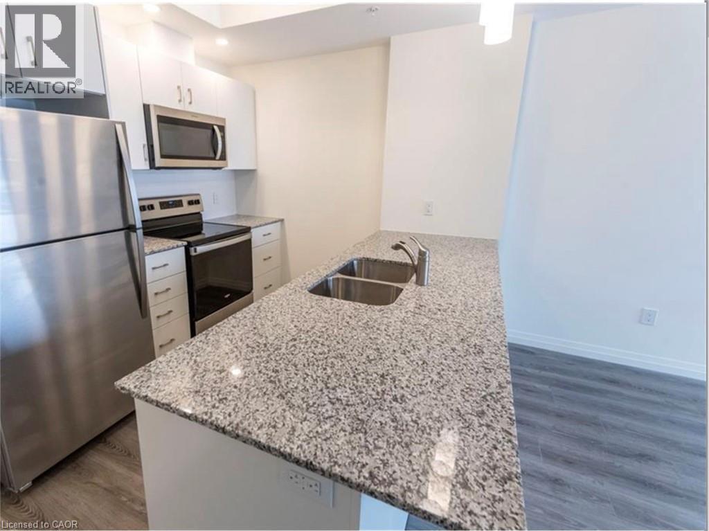 Kitchen featuring appliances with stainless steel finishes, light stone counters, dark wood-style flooring, a peninsula, and white cabinets - 108 Garment Street Unit# 606, Kitchener, ON - Indoor Photo Showing Kitchen With Stainless Steel Kitchen With Double Sink With Upgraded Kitchen