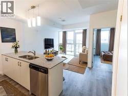Kitchen with stainless steel dishwasher, hanging light fixtures, open floor plan, light stone countertops, and light wood-style flooring -