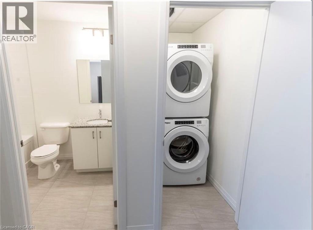 Laundry room featuring stacked washer / drying machine and light tile patterned floors - 108 Garment Street Unit# 606, Kitchener, ON - Indoor Photo Showing Laundry Room
