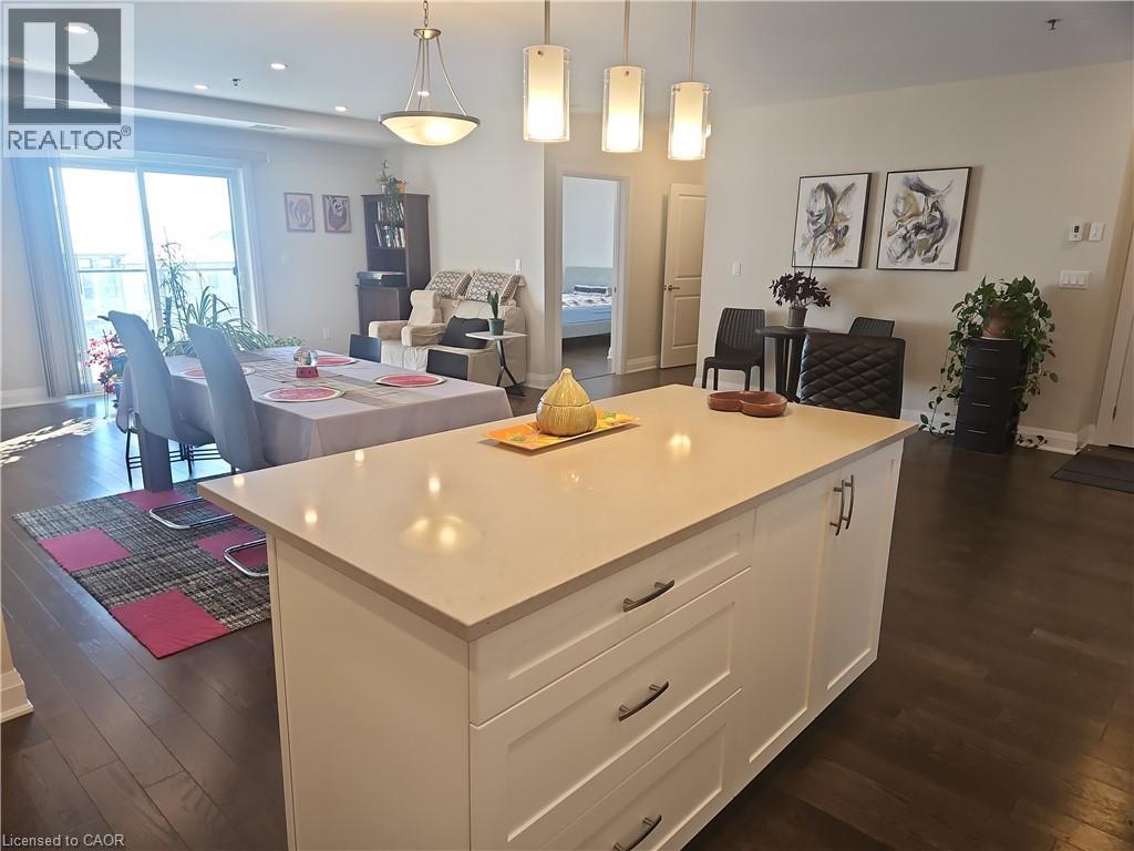 Kitchen featuring open floor plan, dark wood-type flooring, white cabinetry, a kitchen island, and hanging light fixtures - 249 Grey Silo Road Unit# 301, Waterloo, ON - Indoor
