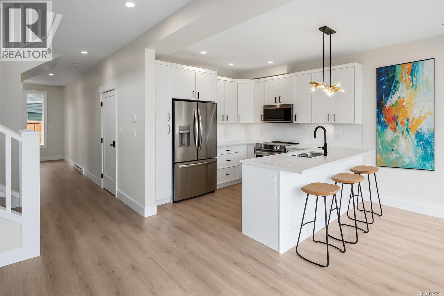 Kitchen featuring appliances with stainless steel finishes, decorative light fixtures, white cabinets, a kitchen breakfast bar, and a peninsula - A 6521 Noblewood Pl, Sooke, BC - Indoor Photo Showing Kitchen With Upgraded Kitchen