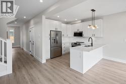 Kitchen featuring a peninsula, stainless steel appliances, white cabinets, decorative light fixtures, and decorative backsplash -