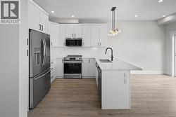 Kitchen featuring stainless steel appliances, tasteful backsplash, white cabinets, a peninsula, and light stone countertops -