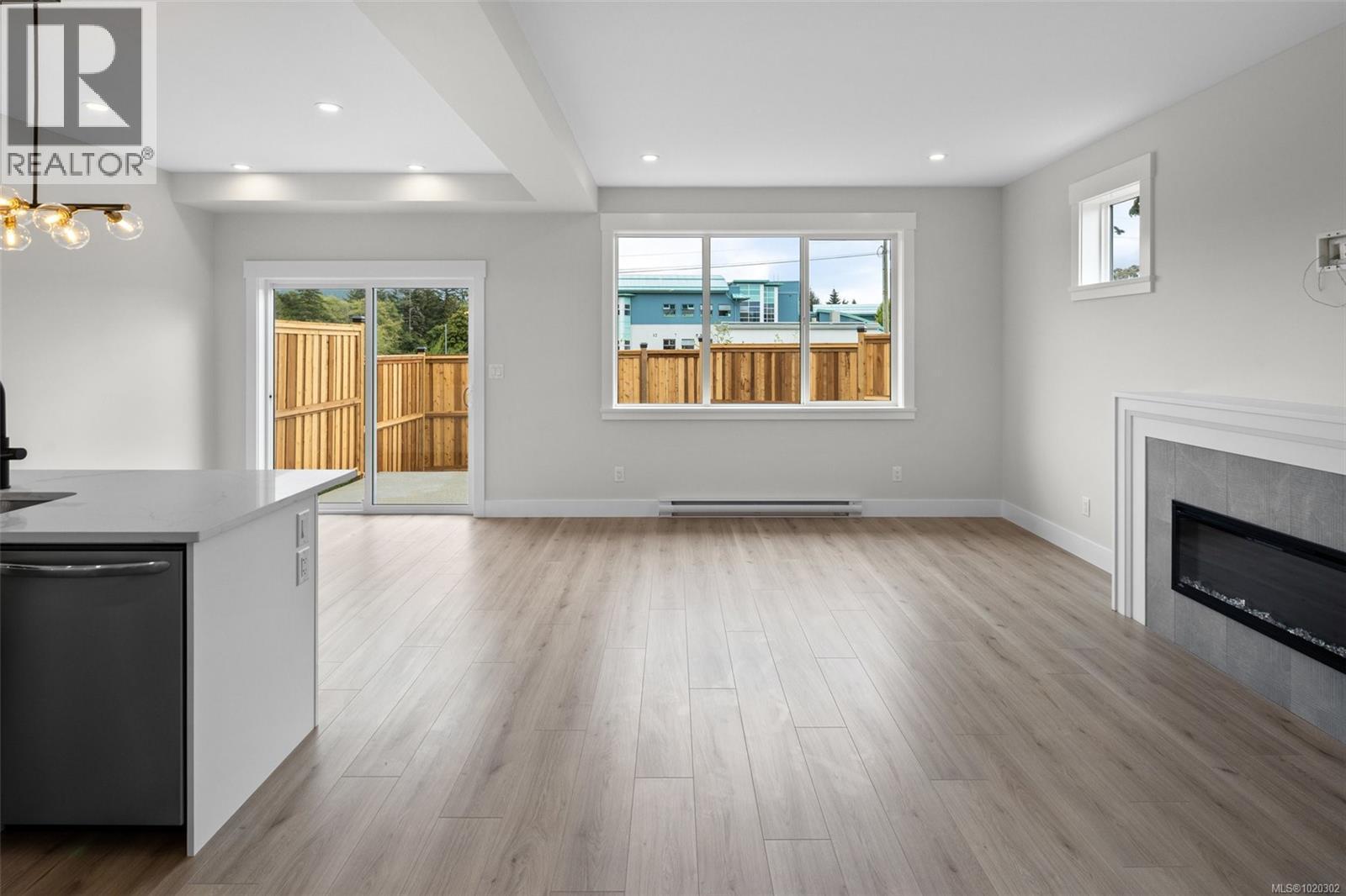 Unfurnished living room with a tiled fireplace, light wood-style flooring, recessed lighting, a baseboard radiator, and a chandelier - A 6521 Noblewood Pl, Sooke, BC - Indoor Photo Showing Living Room With Fireplace