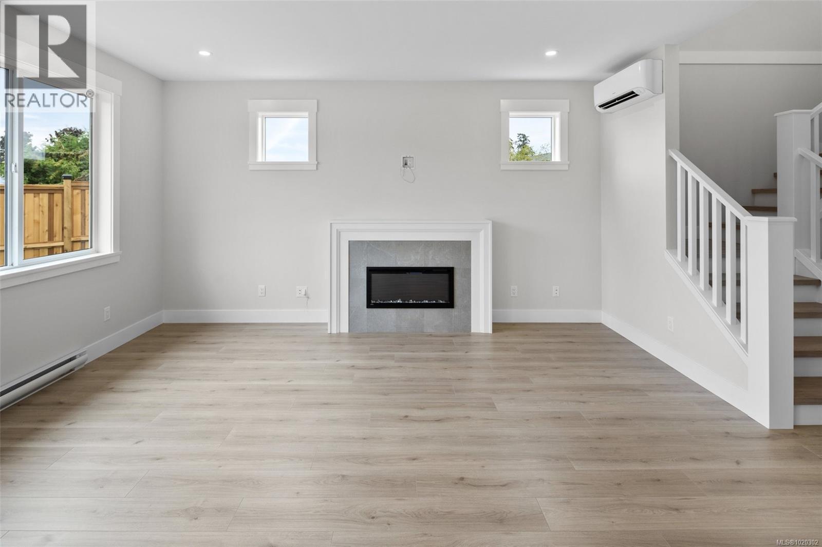 Unfurnished living room with stairs, light wood-style floors, a glass covered fireplace, a wall mounted AC, and recessed lighting - A 6521 Noblewood Pl, Sooke, BC - Indoor Photo Showing Other Room With Fireplace