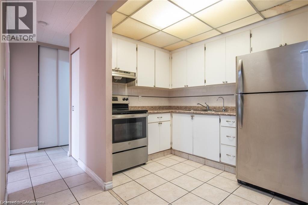 Kitchen featuring appliances with stainless steel finishes, white cabinetry, light tile patterned floors, under cabinet range hood, and a paneled ceiling - 71 Vanier Drive Unit# 211, Kitchener, ON - Indoor Photo Showing Kitchen