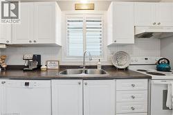 Kitchen with white appliances, backsplash, white cabinetry, and under cabinet range hood -