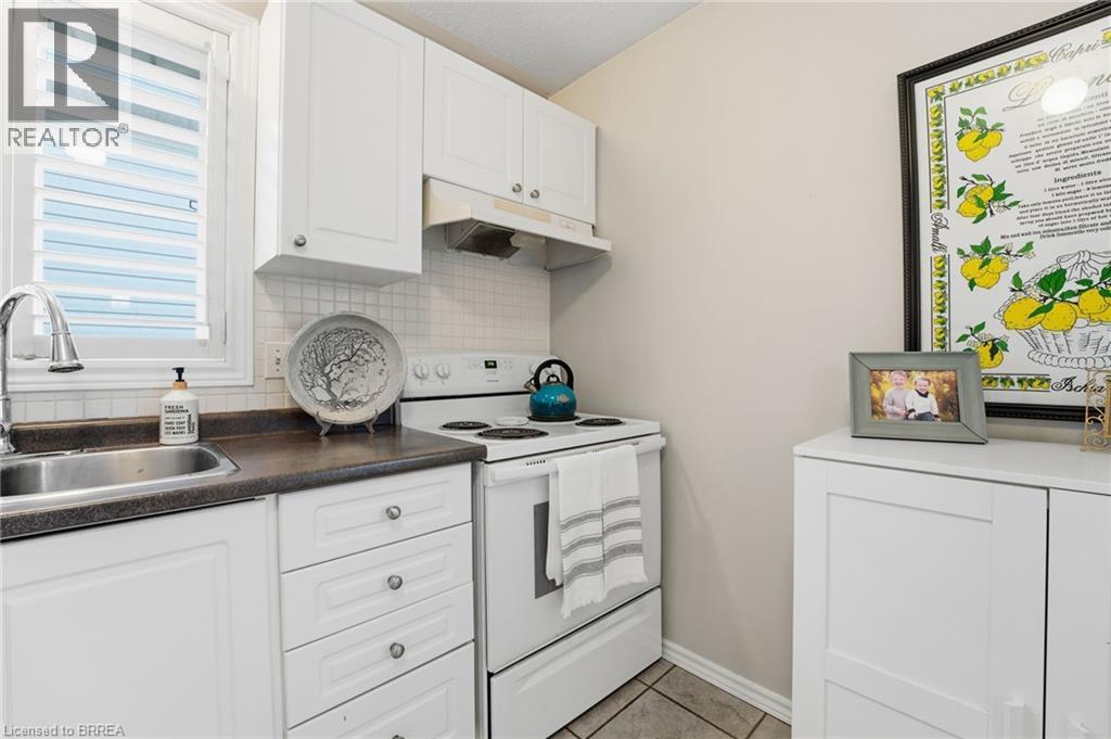 Kitchen with electric range, white cabinetry, under cabinet range hood, decorative backsplash, and light tile patterned floors - 14 Dunton Lane, Paris, ON - Indoor Photo Showing Kitchen