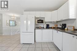 Kitchen featuring white appliances, white cabinets, dark countertops, backsplash, and light tile patterned floors -