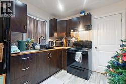 Kitchen featuring dark brown cabinetry, black appliances, ventilation hood, light wood-type flooring, and backsplash -