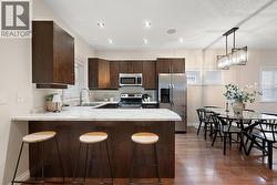 Kitchen featuring a kitchen bar, appliances with stainless steel finishes, dark brown cabinets, a peninsula, and decorative light fixtures -