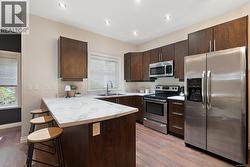 Kitchen featuring stainless steel appliances, a peninsula, a breakfast bar, dark brown cabinets, and light countertops -