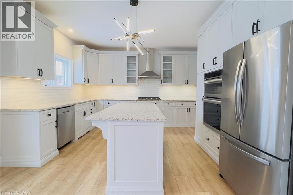Kitchen featuring appliances with stainless steel finishes, white cabinetry, a center island, glass insert cabinets, and wall chimney exhaust hood - 195 Water Street, St. Jacobs, ON - Indoor Photo Showing Kitchen With Upgraded Kitchen