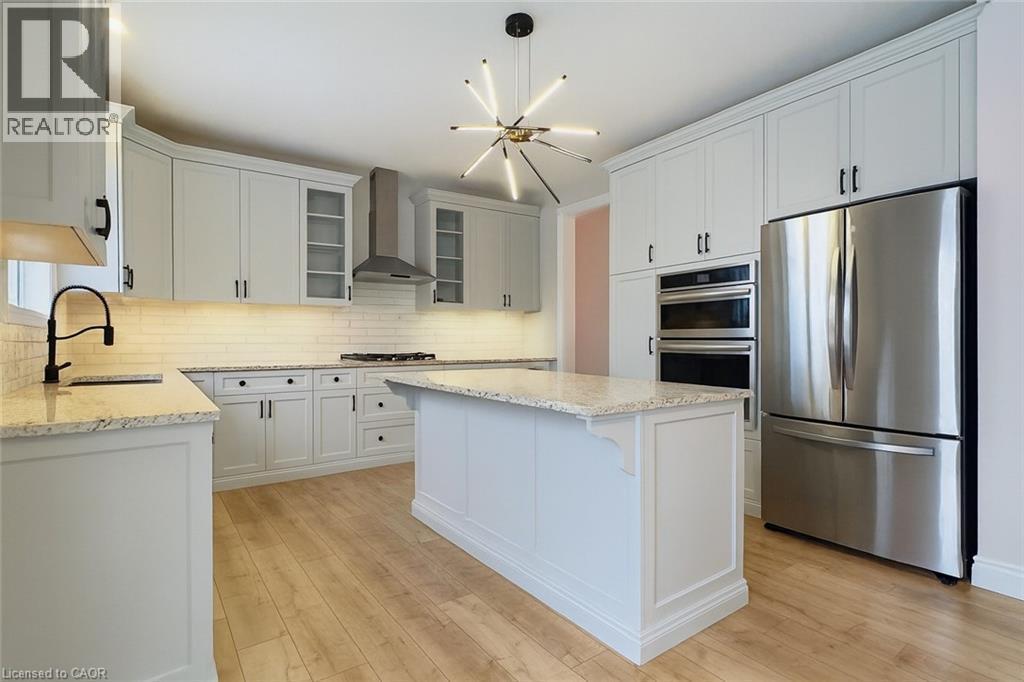 Kitchen with appliances with stainless steel finishes, glass insert cabinets, white cabinets, wall chimney range hood, and light wood finished floors - 195 Water Street, St. Jacobs, ON - Indoor Photo Showing Kitchen With Upgraded Kitchen