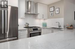Kitchen featuring appliances with stainless steel finishes, wall chimney range hood, light stone counters, white cabinets, and tasteful backsplash -