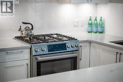 Kitchen featuring tasteful backsplash, stainless steel gas range oven, white cabinets, and light stone countertops -