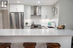 Kitchen featuring a kitchen bar, appliances with stainless steel finishes, wall chimney exhaust hood, and white cabinets -
