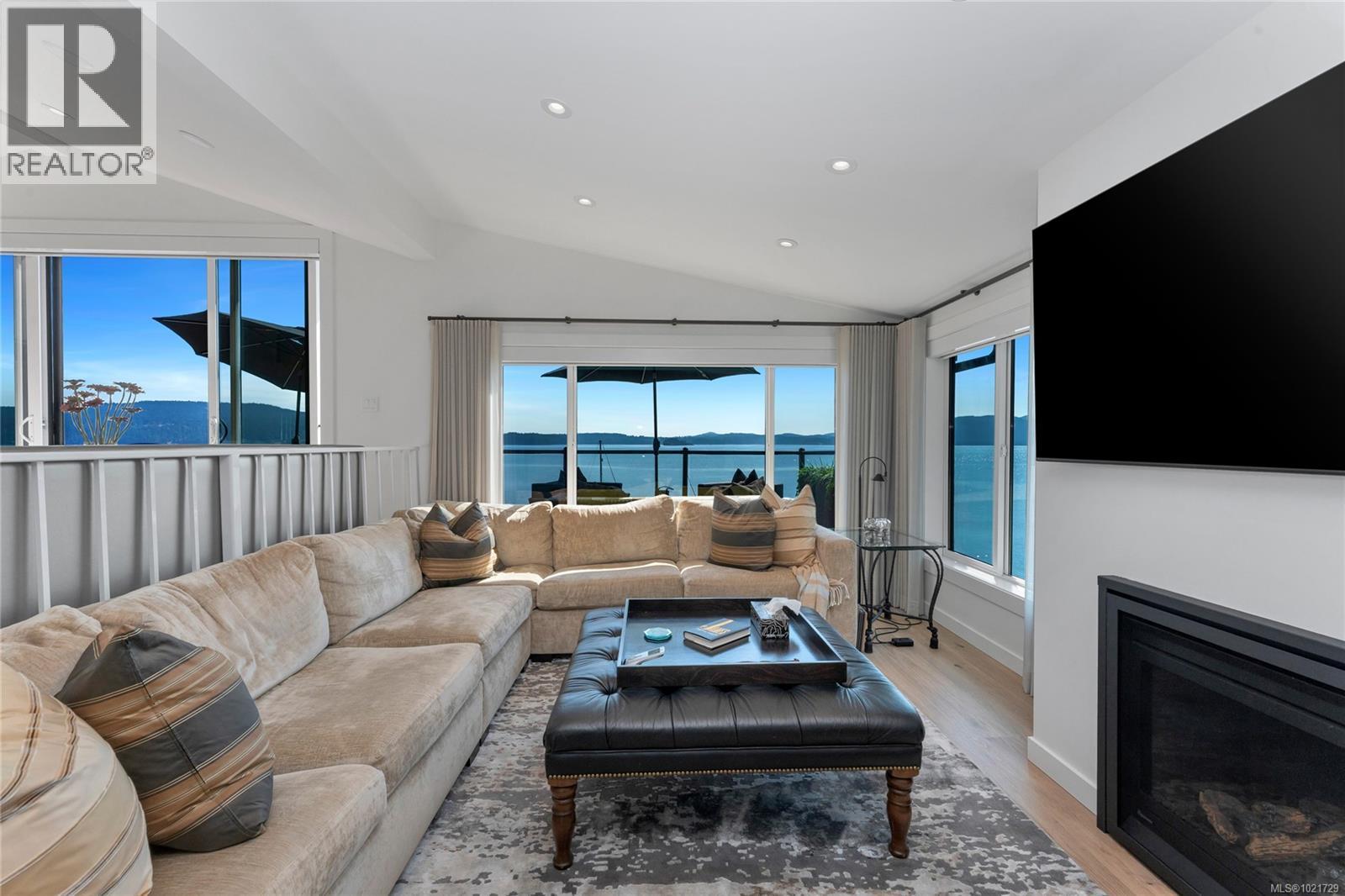 Sunken living room features vaulted ceiling, fireplace and wide-open water views - 4 1723 Sandy Beach Rd, Mill Bay, BC - Indoor Photo Showing Living Room With Fireplace