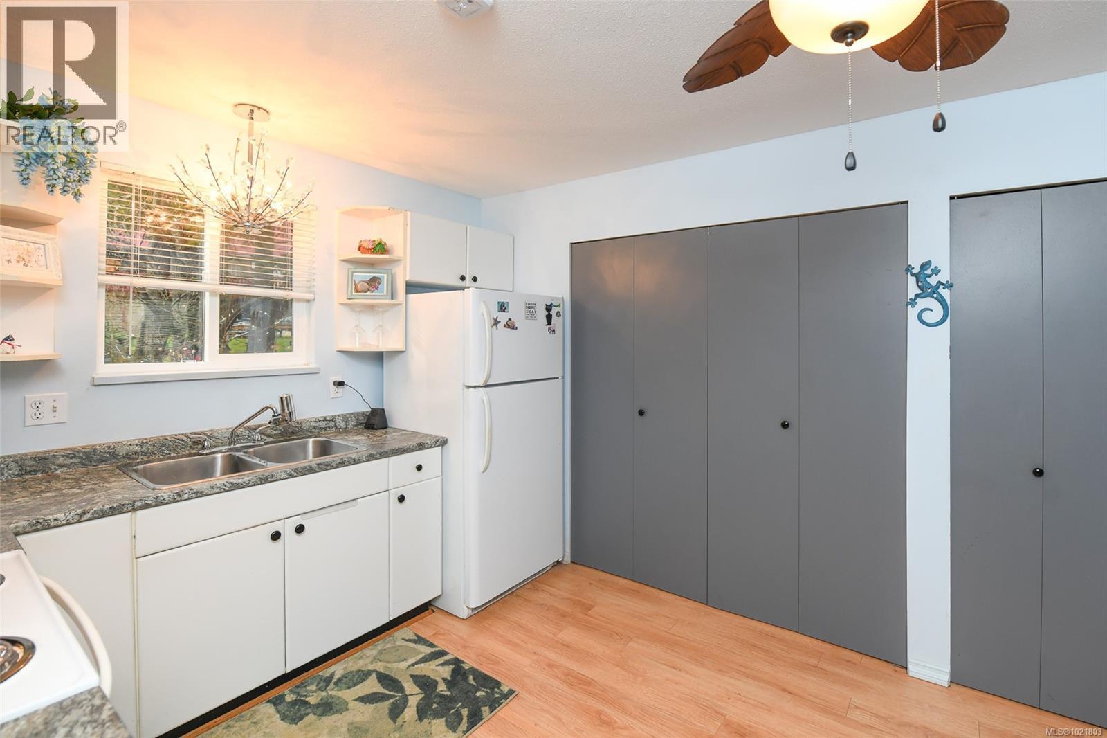 Kitchen featuring dark countertops, open shelves, white cabinetry, white appliances, and light wood-type flooring - 31 1535 Dingwall Rd, Courtenay, BC - Indoor Photo Showing Kitchen With Double Sink