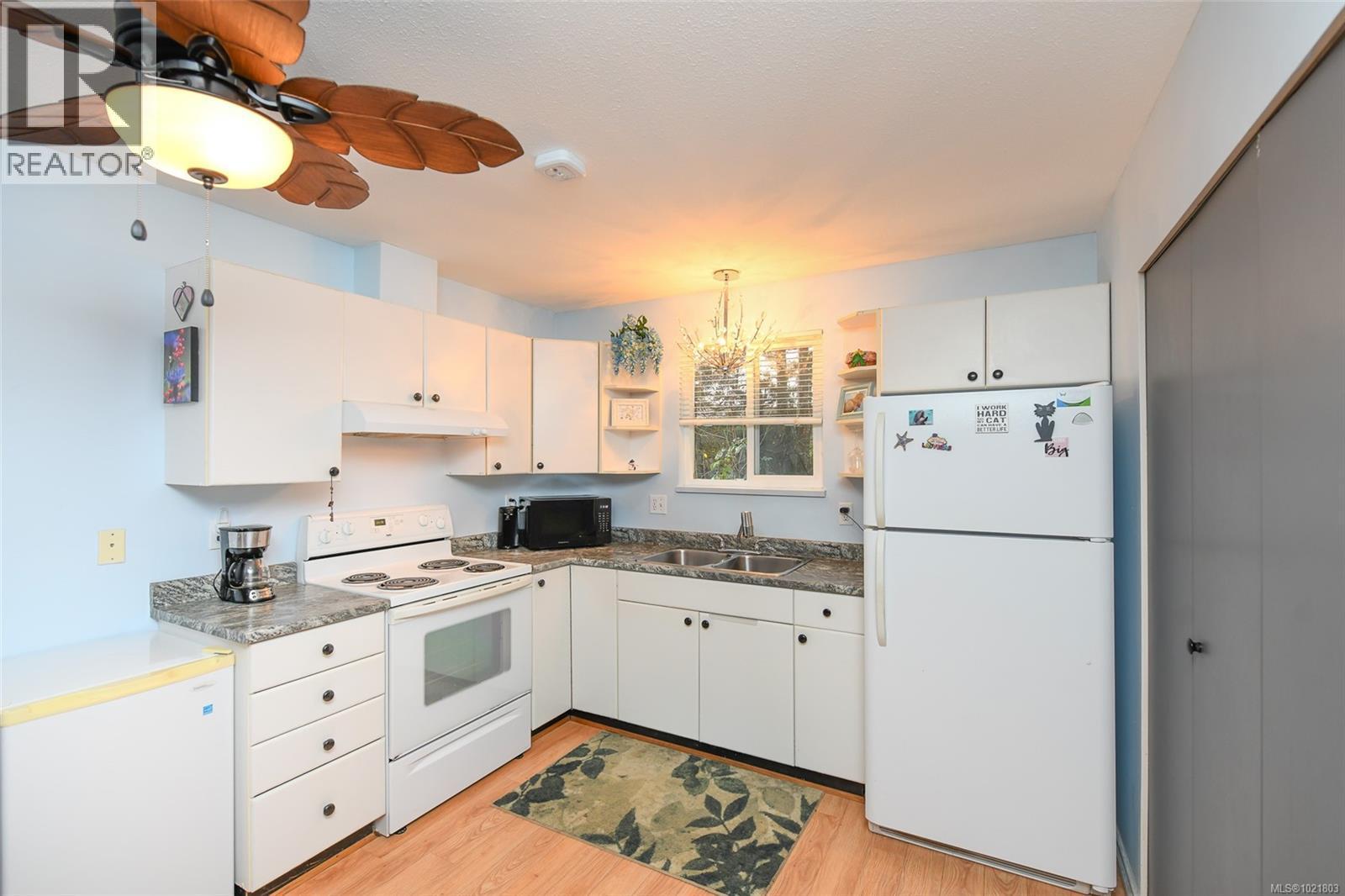 Kitchen featuring white appliances, white cabinets, open shelves, decorative light fixtures, and light wood-style flooring - 31 1535 Dingwall Rd, Courtenay, BC - Indoor Photo Showing Kitchen With Double Sink