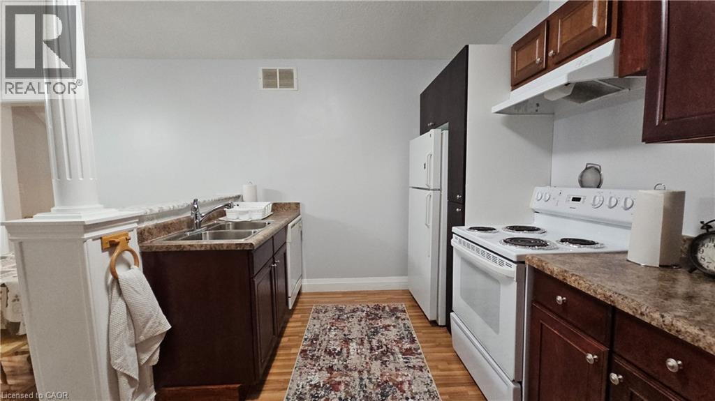 Kitchen featuring dark brown cabinetry, white appliances, under cabinet range hood, light wood-type flooring, and a peninsula - 10 Doll Court Unit# Lower, Kitchener, ON - Indoor Photo Showing Kitchen With Double Sink