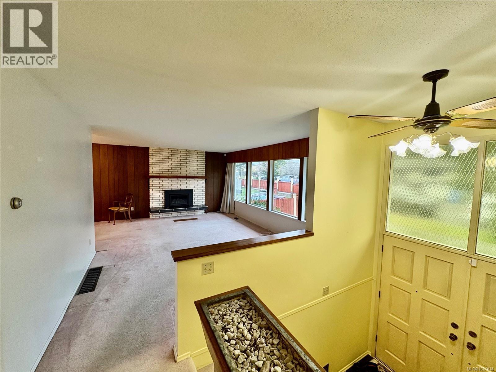 Living area with wooden walls, a brick fireplace, a ceiling fan, carpet floors, and a textured ceiling - 2738 14Th Ave, Port Alberni, BC - Indoor Photo Showing Other Room With Fireplace