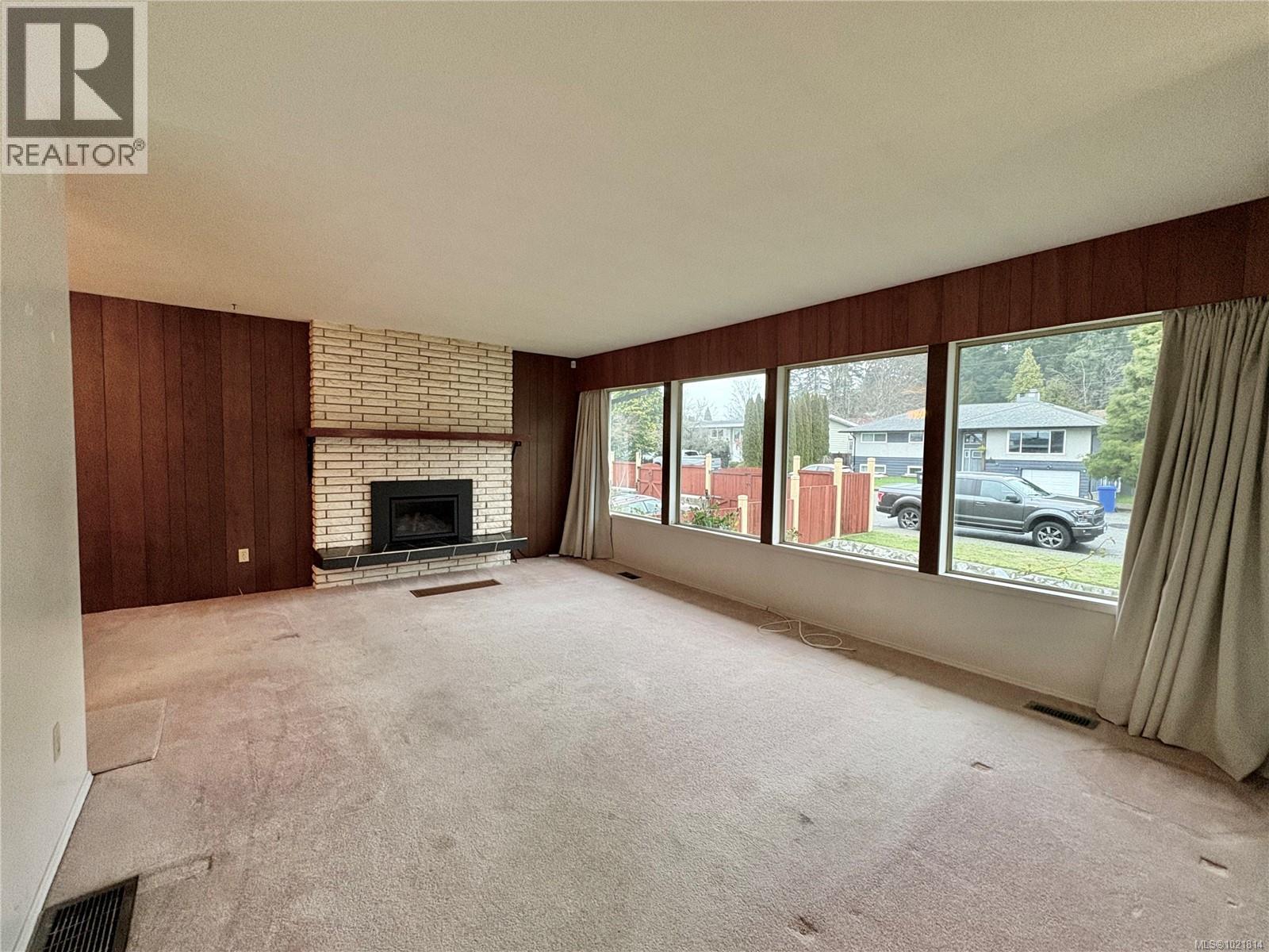 Unfurnished living room featuring wood walls, a brick fireplace, and carpet flooring - 2738 14Th Ave, Port Alberni, BC - Indoor Photo Showing Living Room With Fireplace