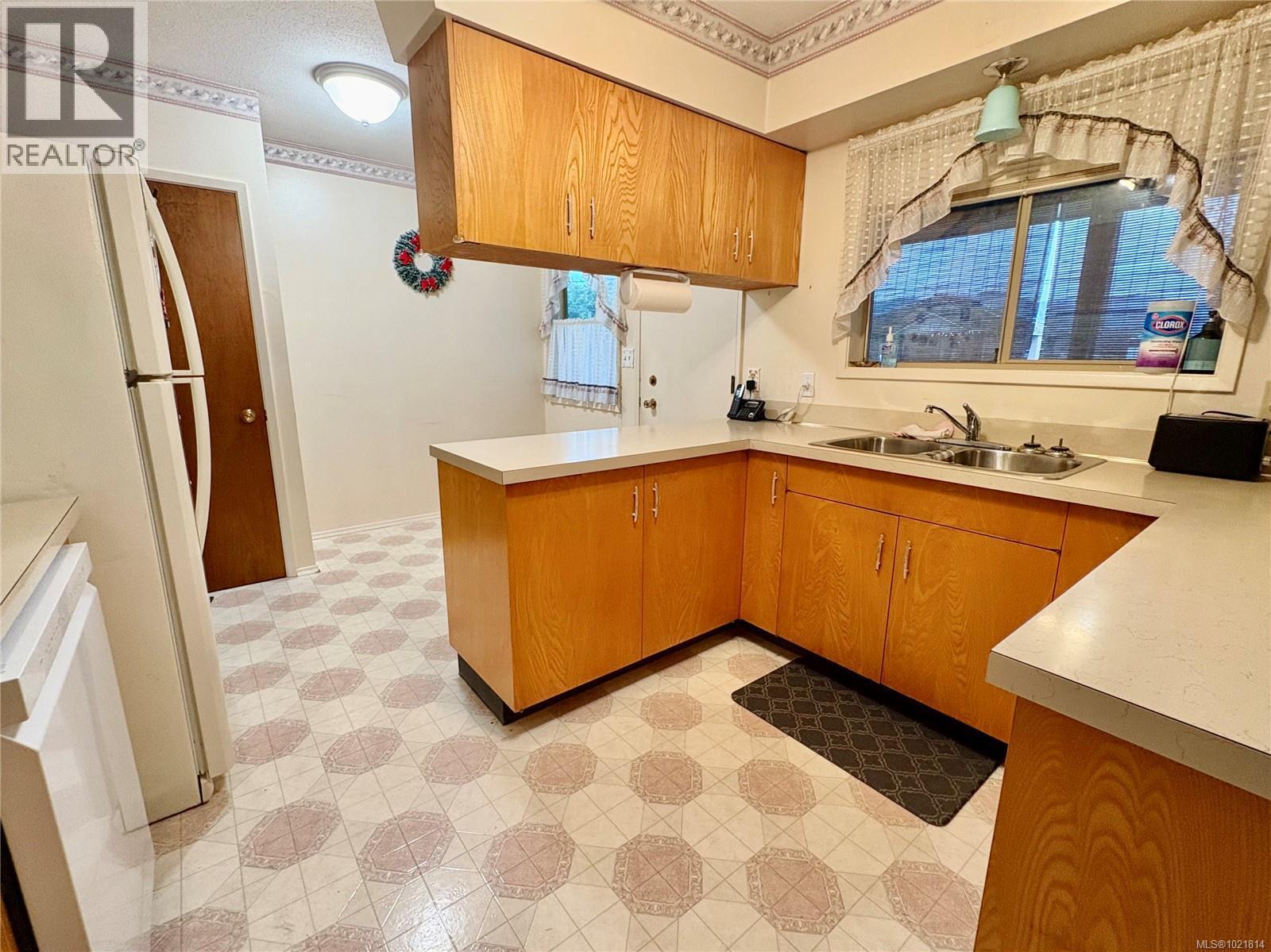 Kitchen with brown cabinets, light countertops, a peninsula, light floors, and white appliances - 2738 14Th Ave, Port Alberni, BC - Indoor Photo Showing Kitchen With Double Sink