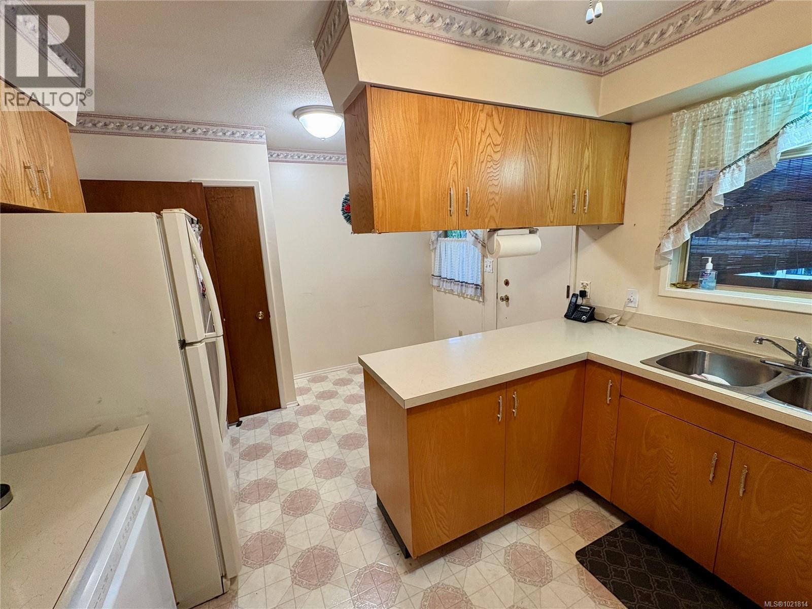 Kitchen featuring light flooring, brown cabinets, a peninsula, light countertops, and healthy amount of natural light - 2738 14Th Ave, Port Alberni, BC - Indoor Photo Showing Kitchen With Double Sink