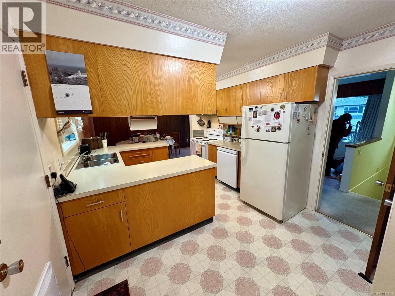 Kitchen with light flooring, brown cabinets, white appliances, light countertops, and wood walls - 2738 14Th Ave, Port Alberni, BC - Indoor Photo Showing Kitchen With Double Sink